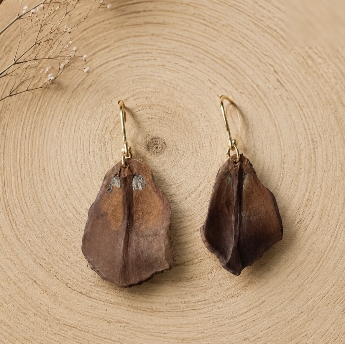 Handmade brown leaf earrings with gold-tone hooks on a cut wood surface