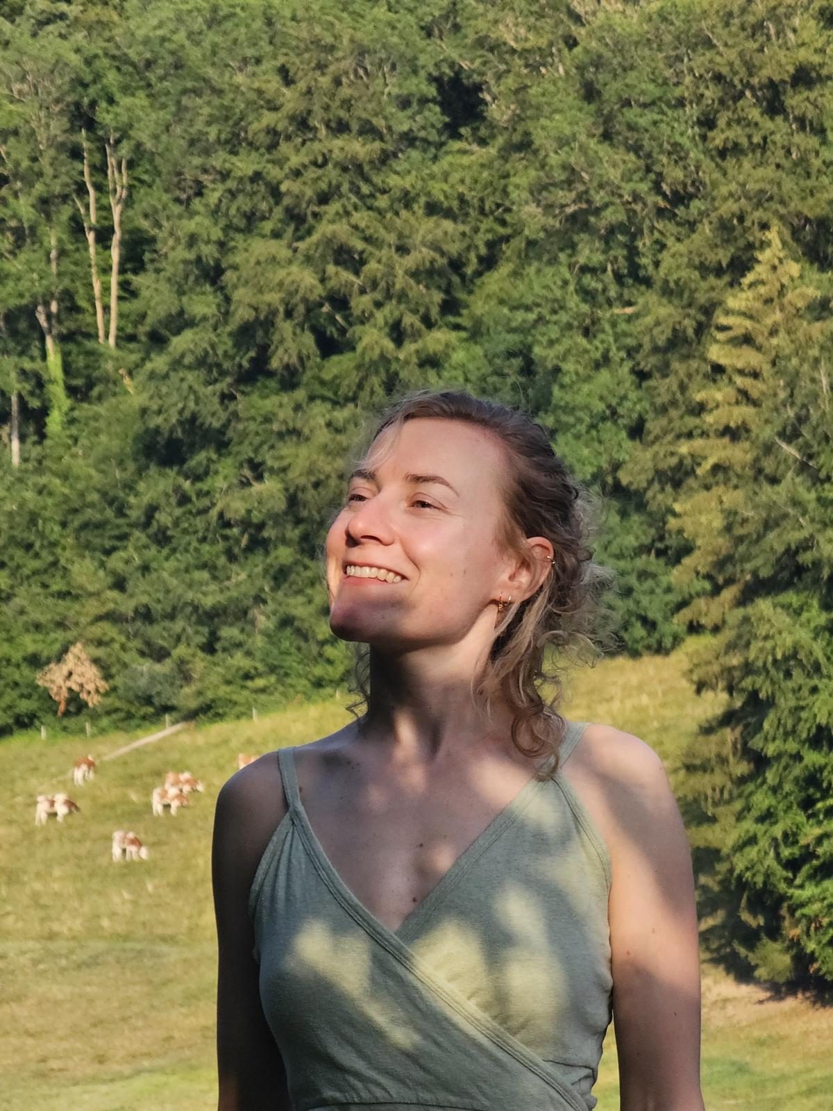 Janina lächelt in der Abendsonne auf einer Wiese vor einem Wald